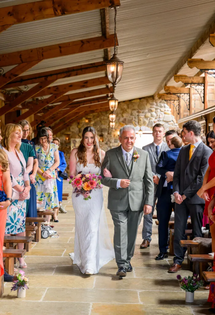 Bride walking down the aisle with her father during barn wedding ceremony