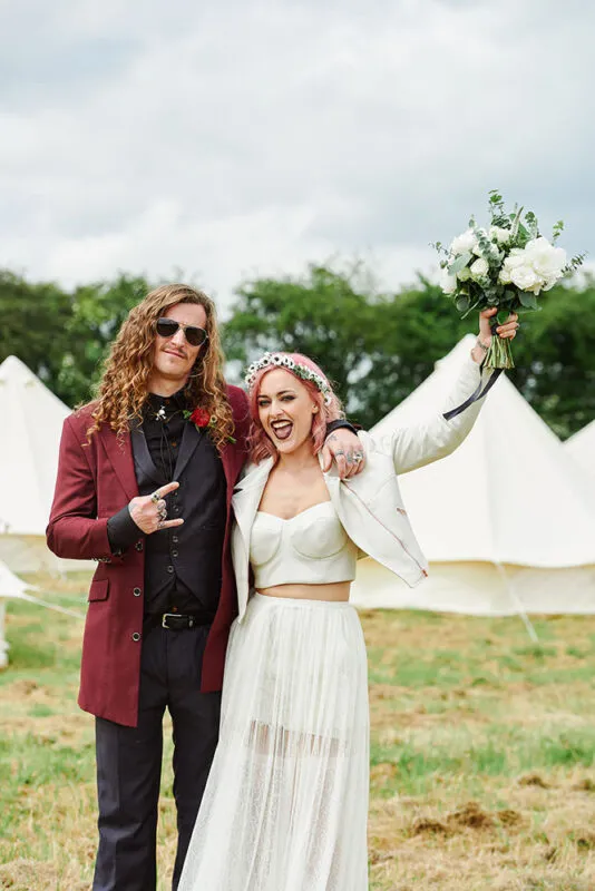 Rock ’n’ roll bride and groom celebrating in front of festival tipis at The Peasantry Brewery, Nottingham