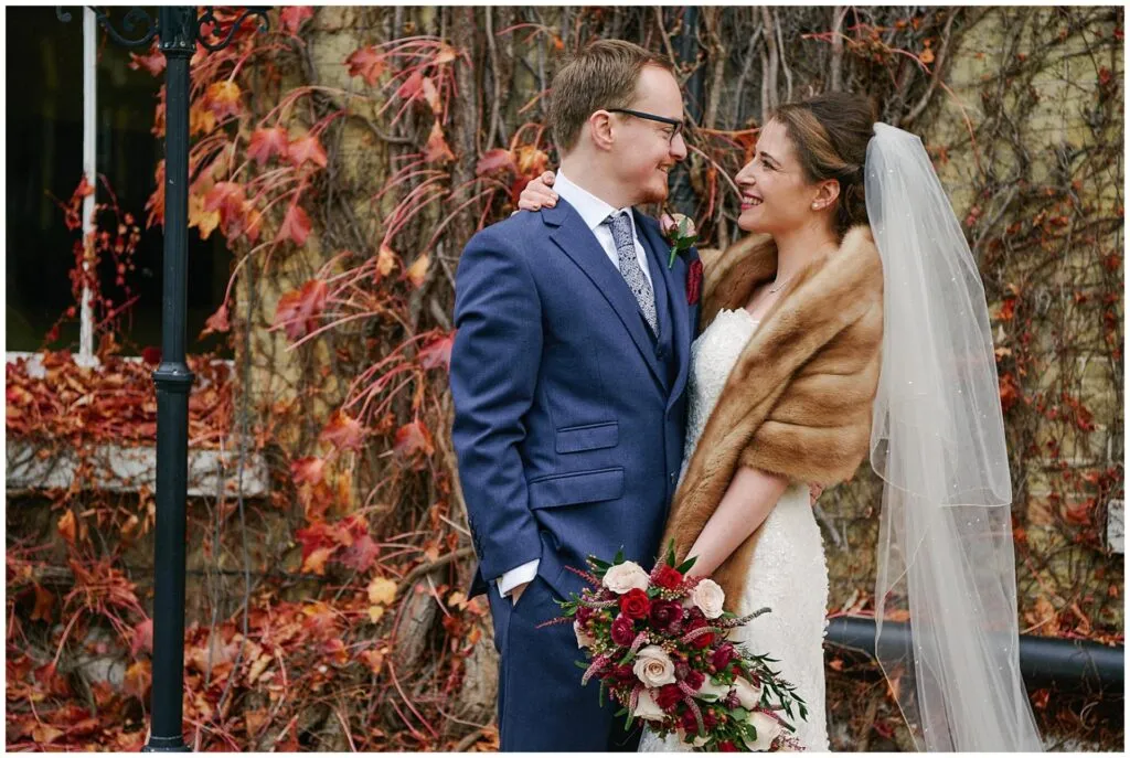 bride and groom smiling in front of red leaves during fun winter wedding