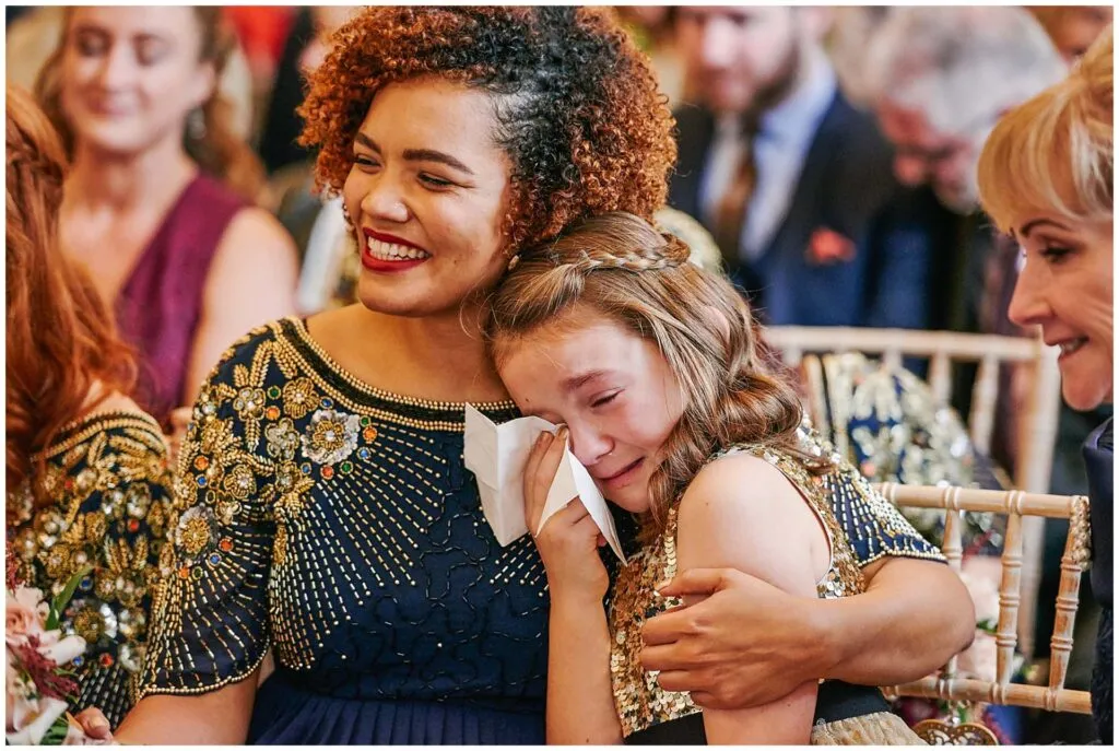 emotional flower girl crying whilst bridesmaid holds her during wedding ceremony