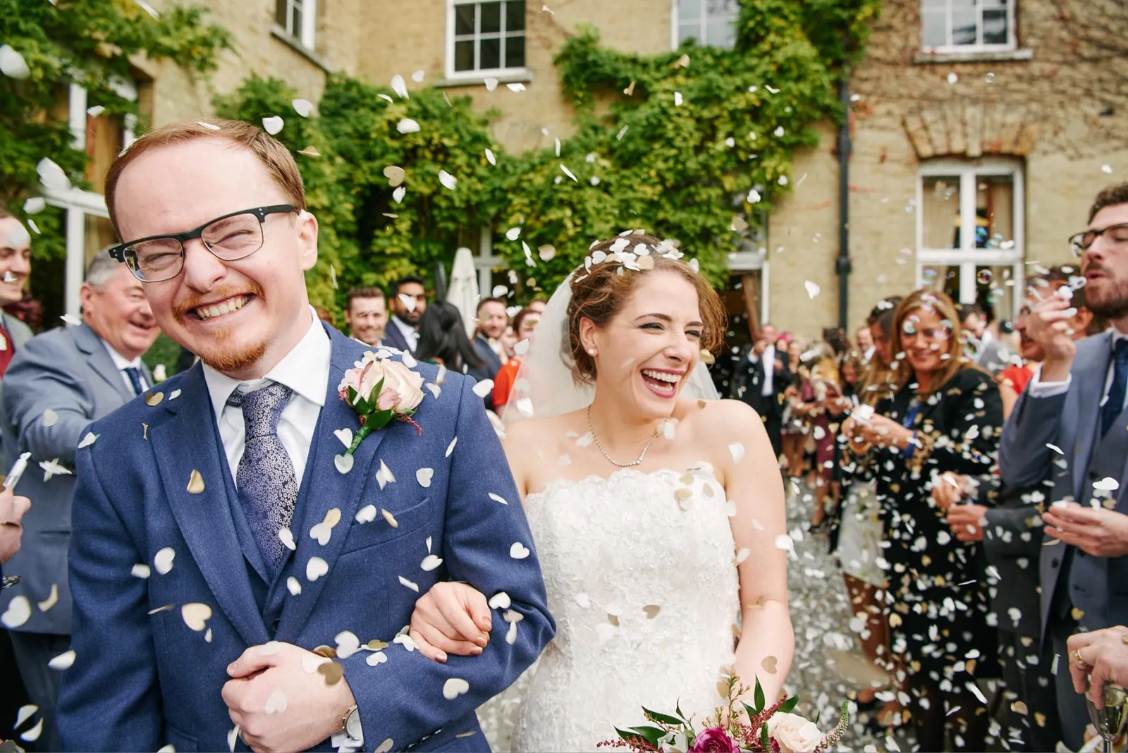 Happy bride and groom laughing whist friends and family throw confetti