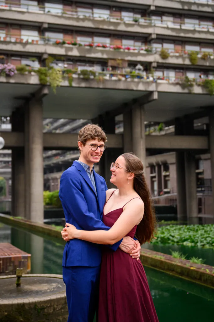 happy couple hugging whilst stood The Barbican Centre for engagement photoshoot