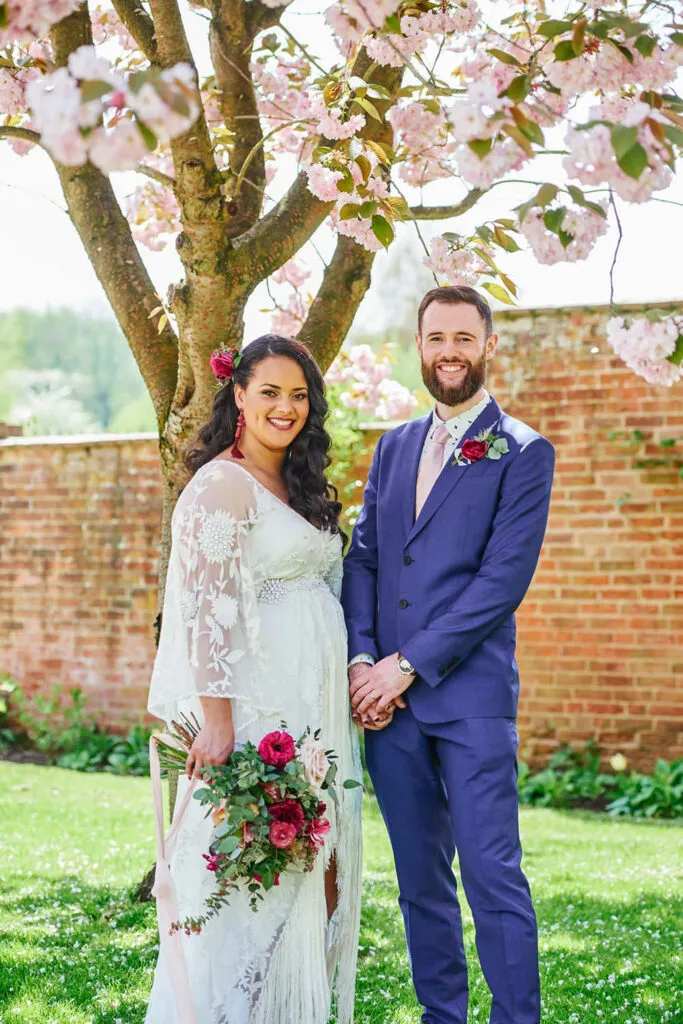 Happy wedding couple stood in front of a cherry blossom tree during wedding photography portraits