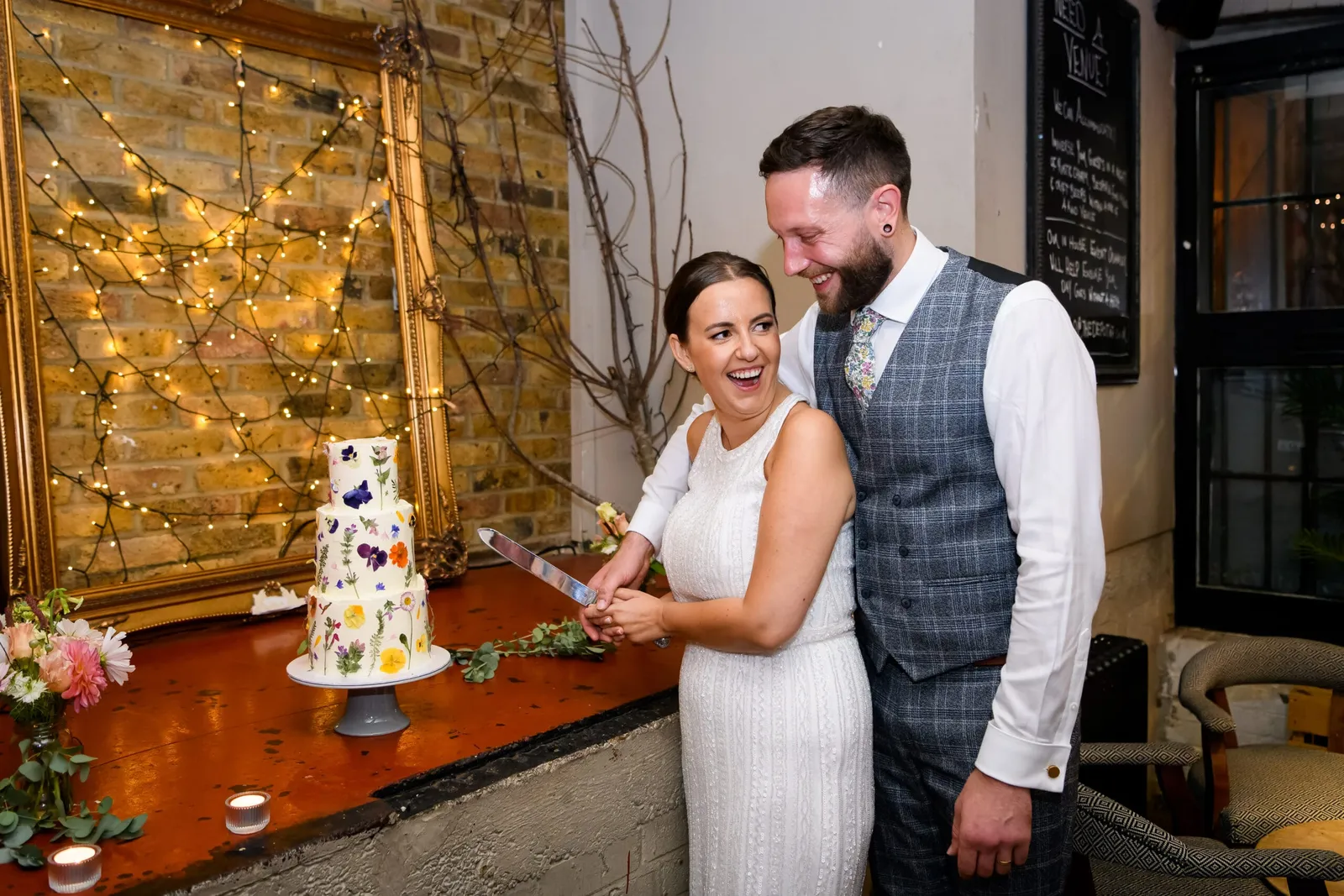 bride and groom cutting flower wedding cake in rustic London pub venue