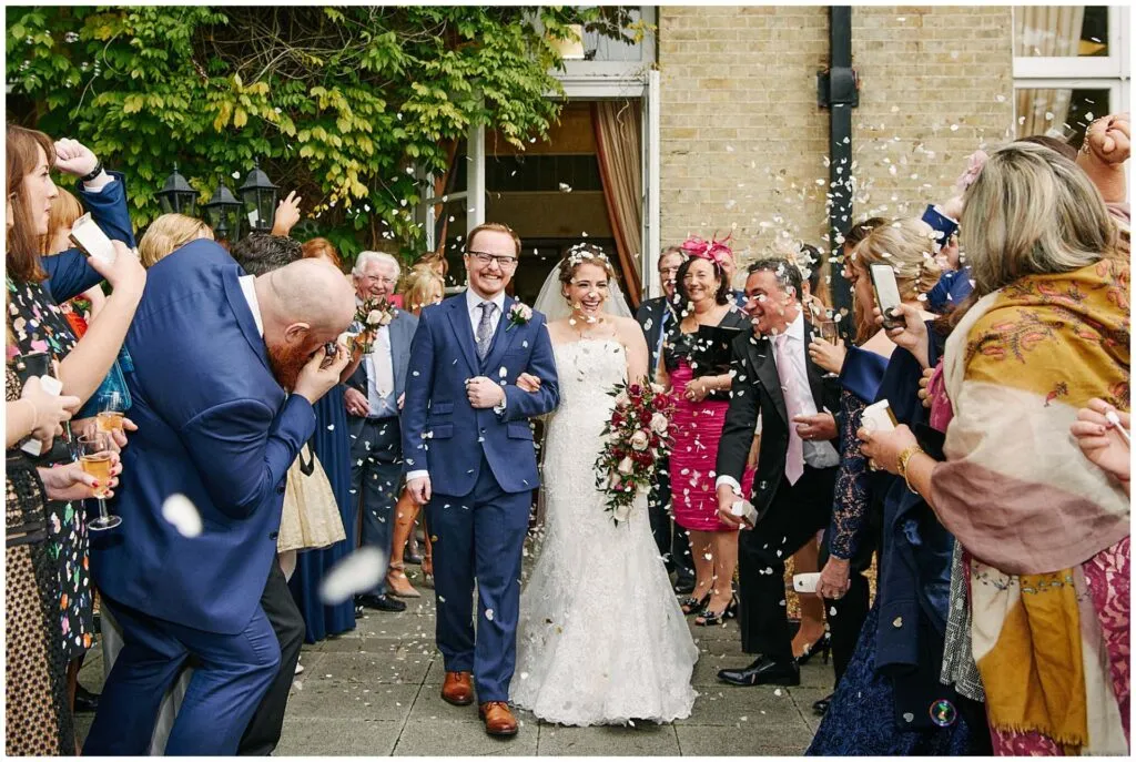 Happy bride and groom exiting wedding venue to family and friends throwing confetti