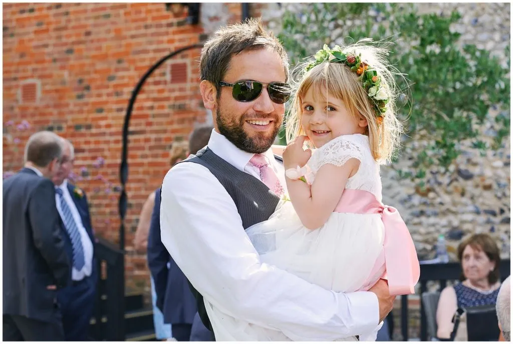 Relaxed wedding photography showing a man and daughter smiling in front of brick wall