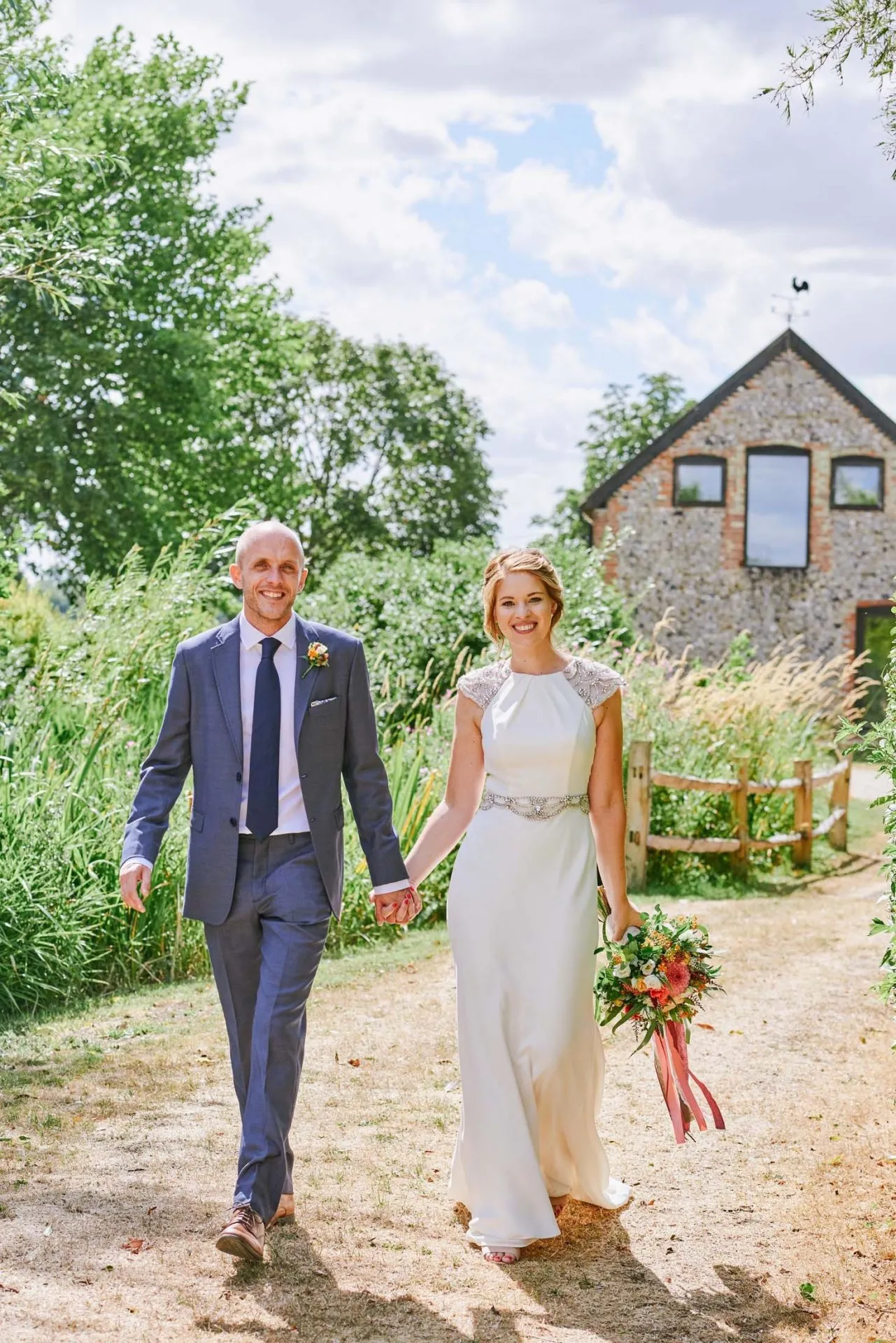 bride and groom walking together on sunny day in front of brick barn