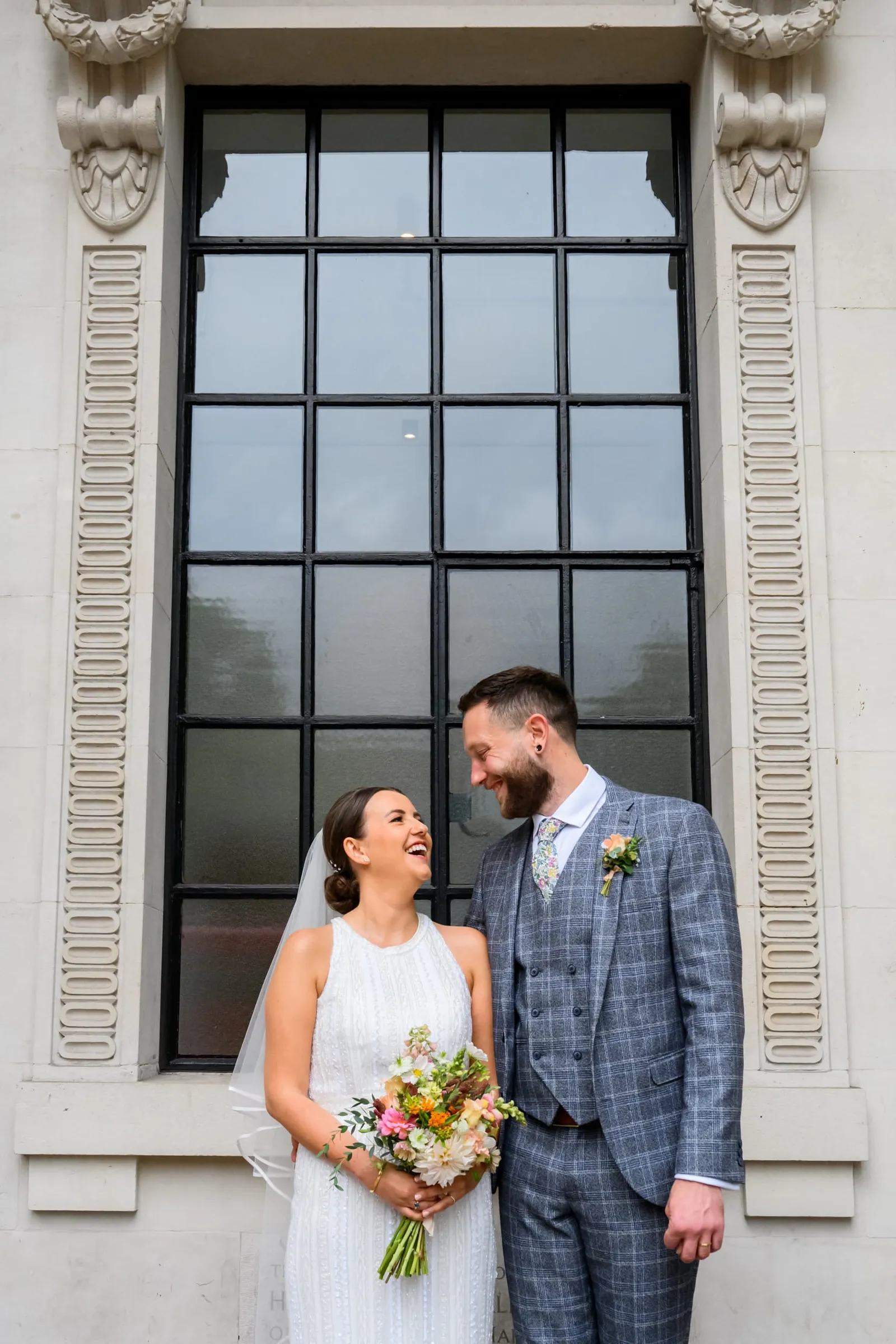 happy bride and groom in front of black framed window during london wedding