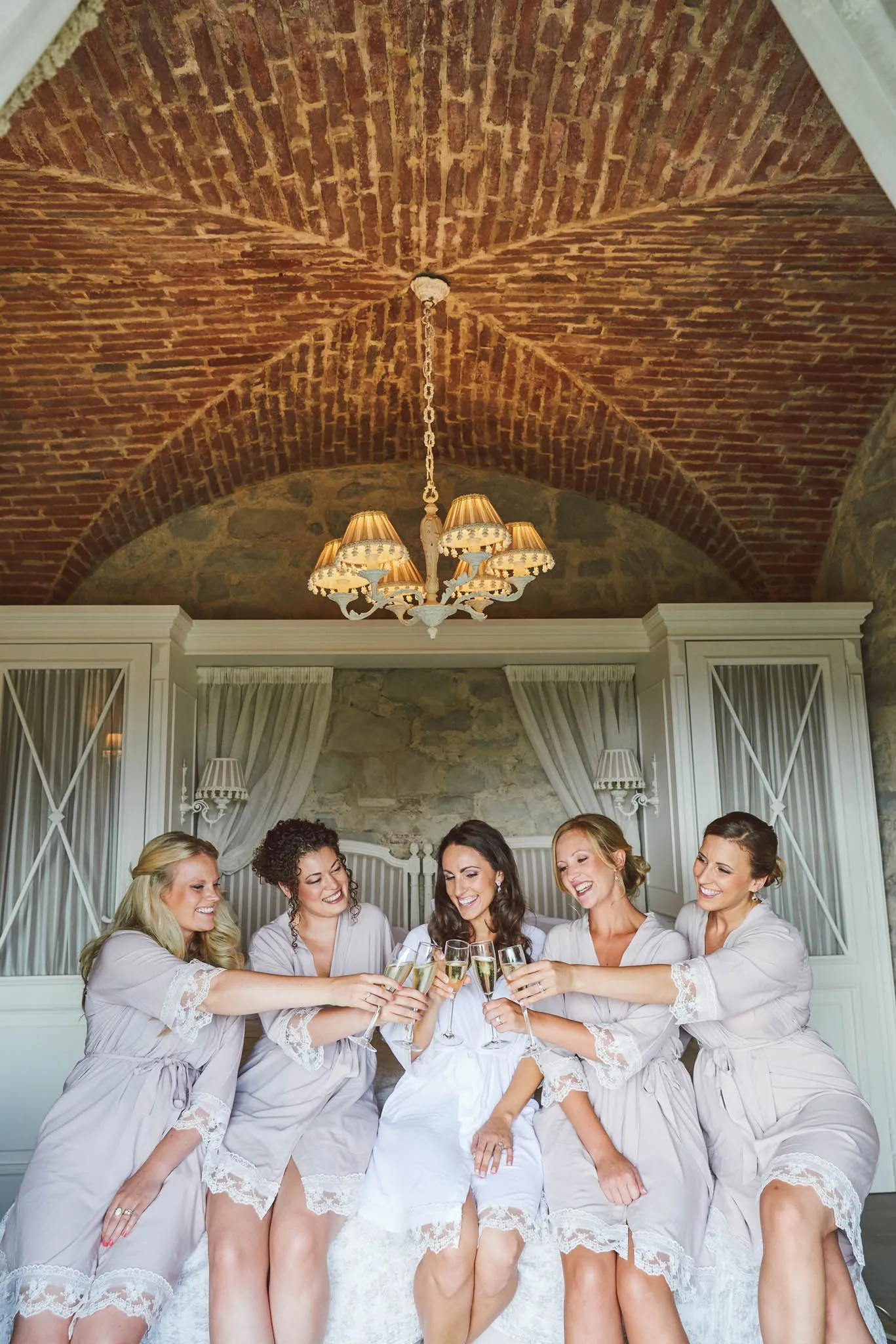bridesmaids in dressing gowns toasting champagne in a rustic brick room