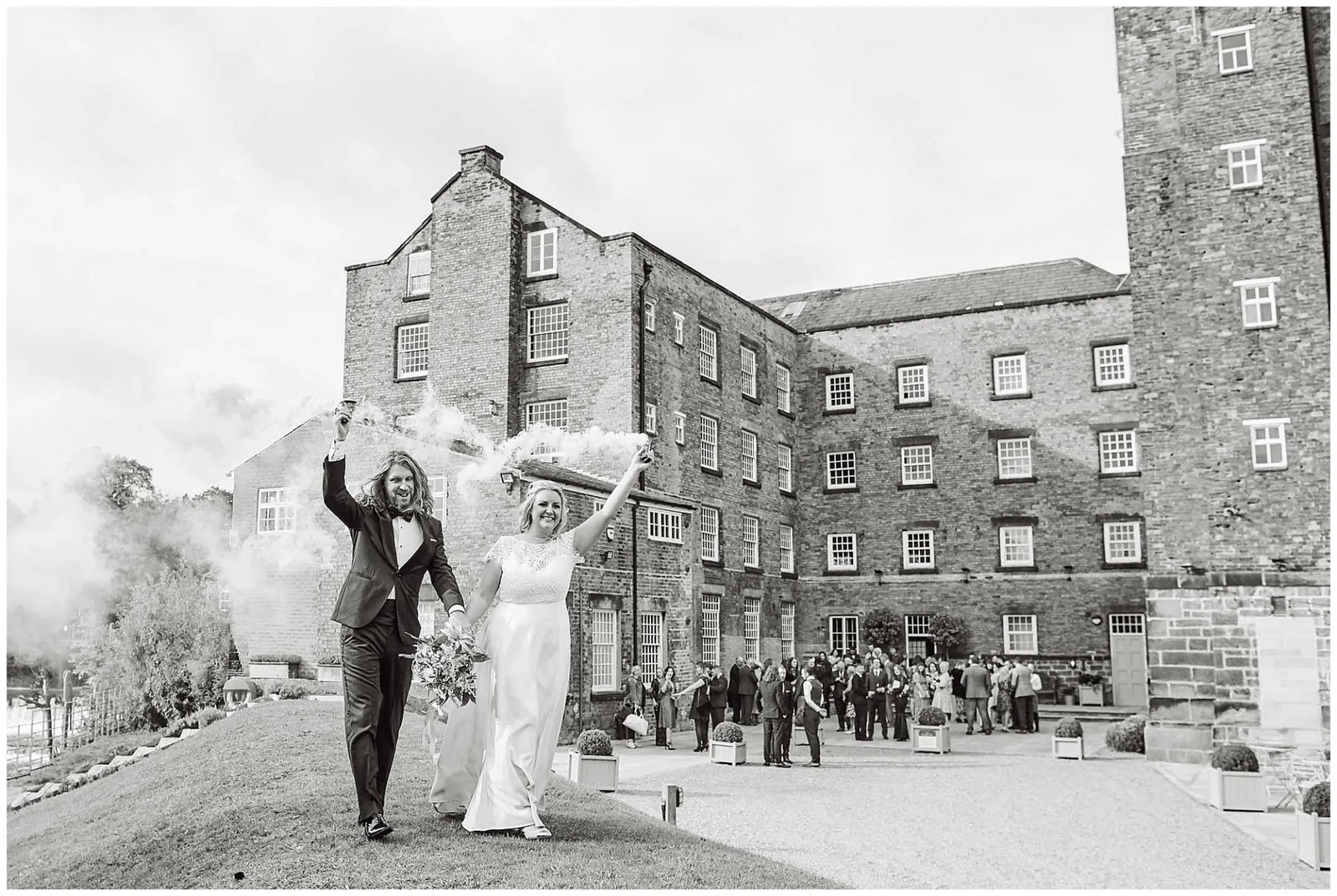 Bride and grrom walking with smoke bombs in front of the west mill wedding venue