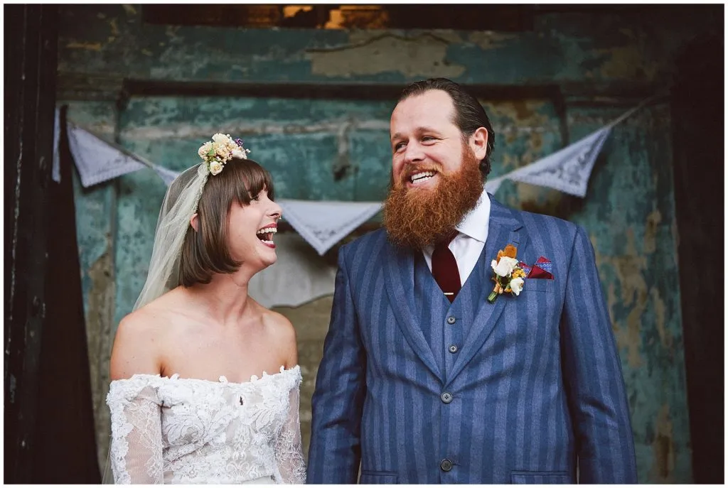 Bride and groom smiling together in front of a blue decaying wall at the Asylum in Peckham.