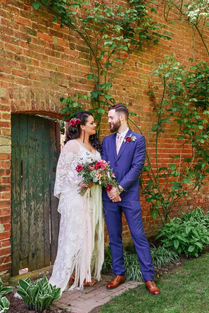 Bride and groom looking at each other in front of brick wall in secret garden