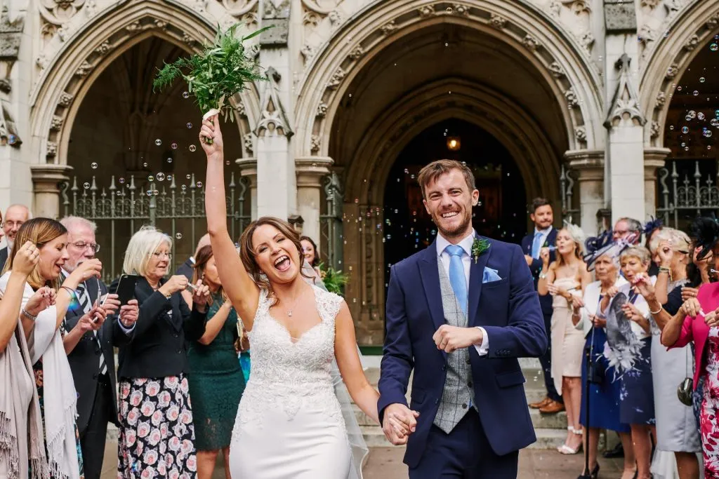 Bride and groom celebrating whilst walking through bubbles outside of St Margaret's Church