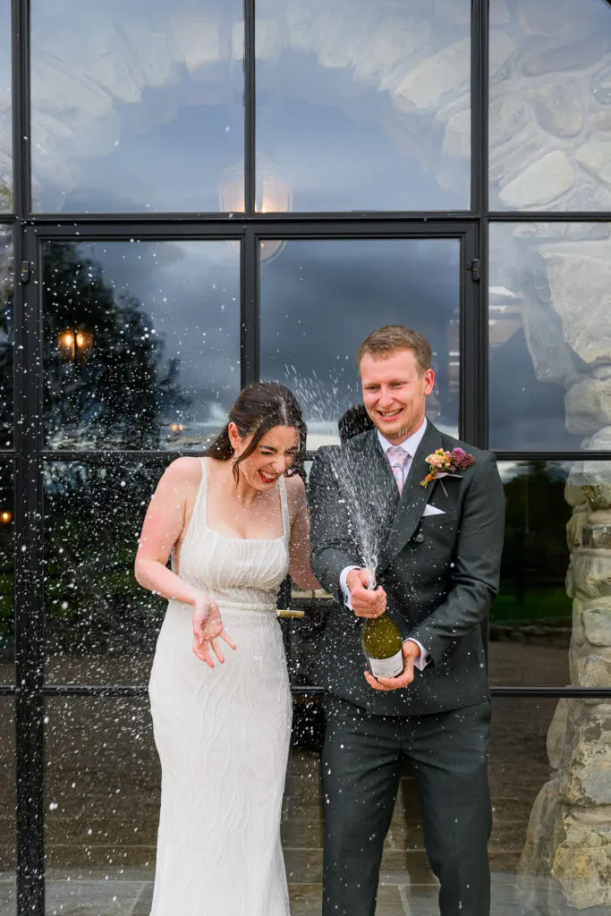 Bride and groom laughing while popping champagne after their wedding