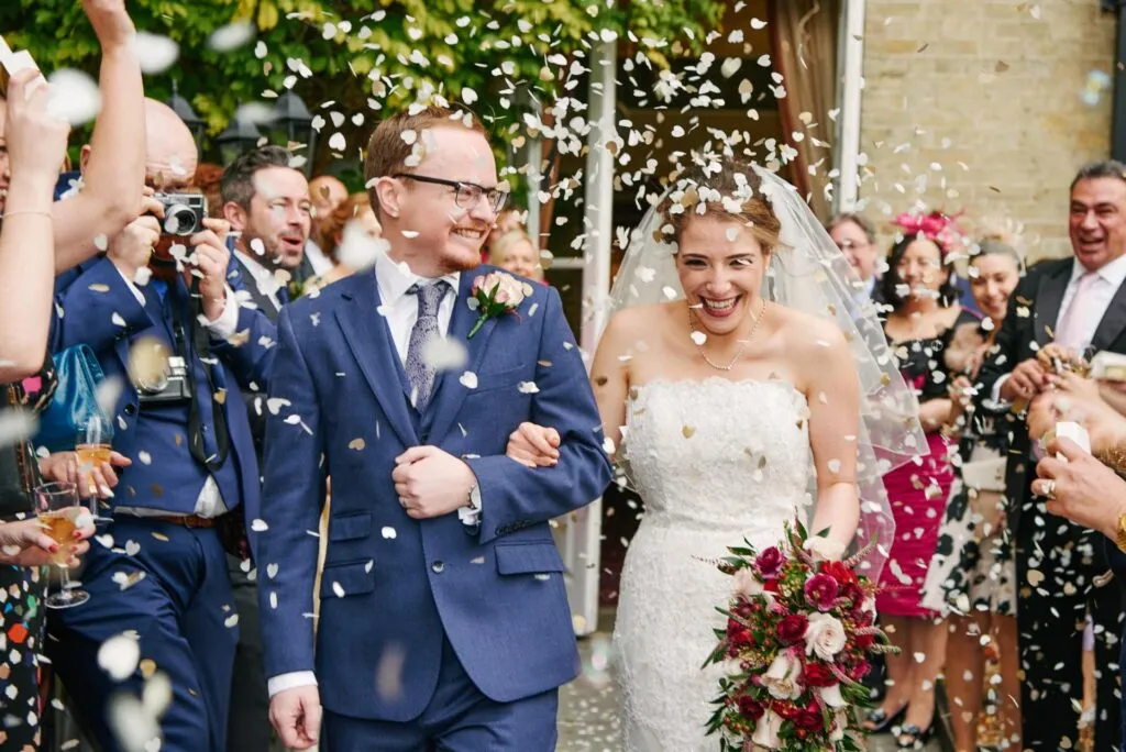 Happy bride and groom laughing whist friends and family throw confetti 