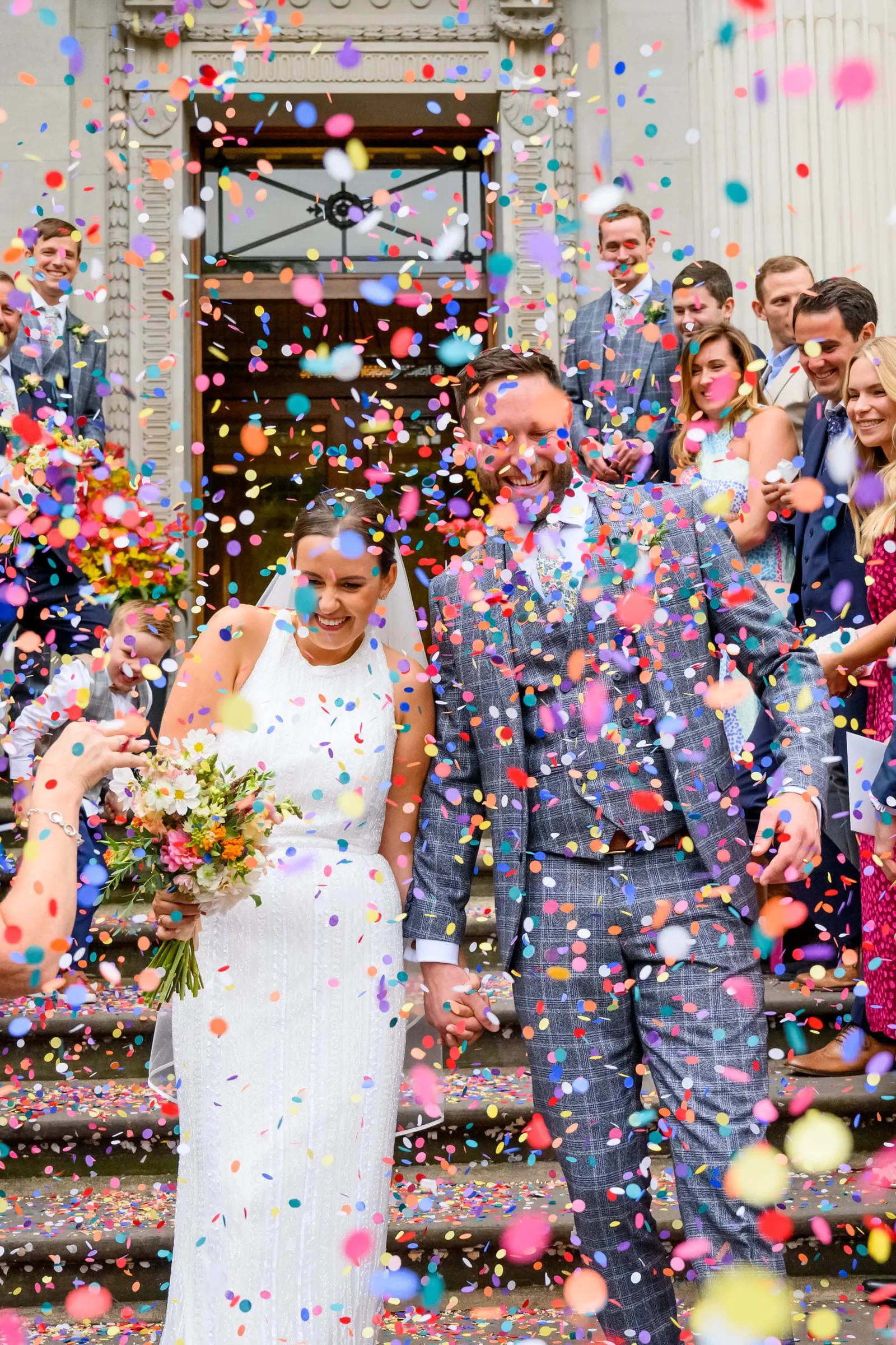 Bride and groom laughing whilst confetti is thrown at them outside town hall