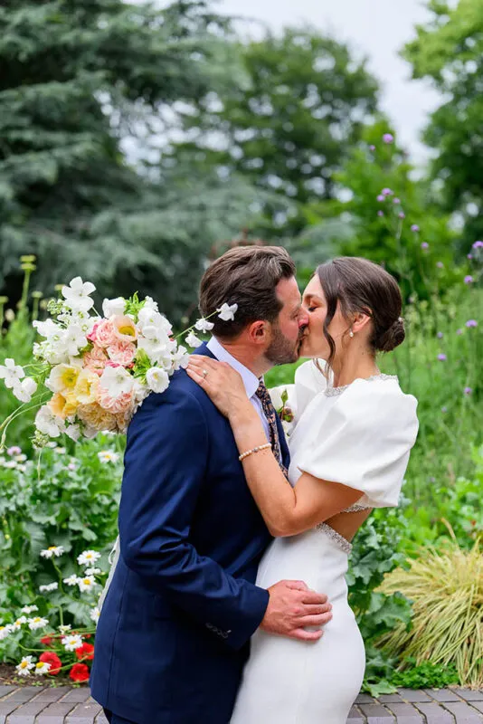 Bride and groom kissing in front of flowers in West Bridgford park
