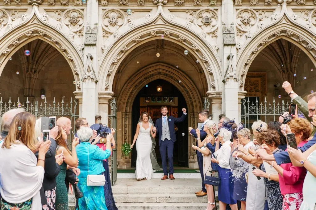 Bride and groom leaving St Margaret's Church whilst they walk through bubble confetti