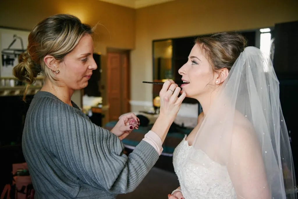 bride having her lipstick applied by makeup artist during london wedding