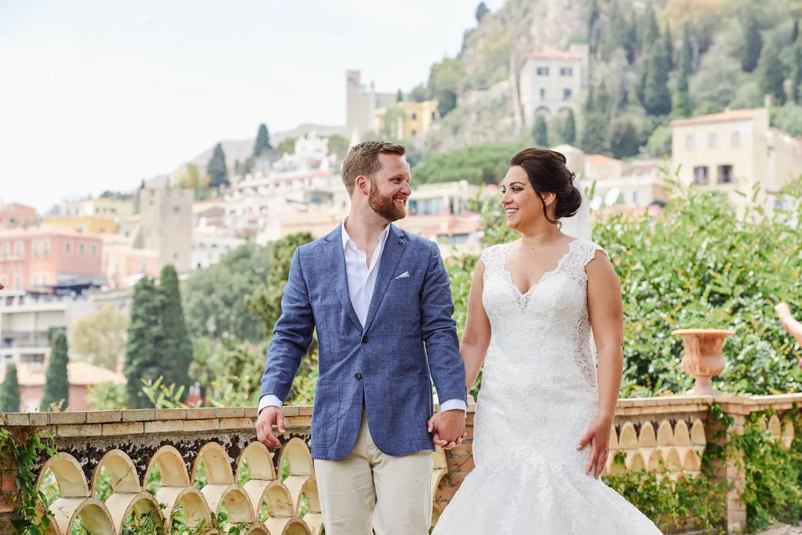 Bride and groom laughing together whilst walking with stunning views of Taormina, Sicily behind them