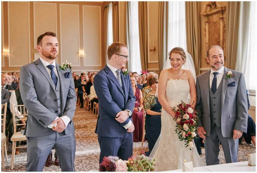 bride and groom smiling whilst surrounded by family and friends during fun wedding ceremony