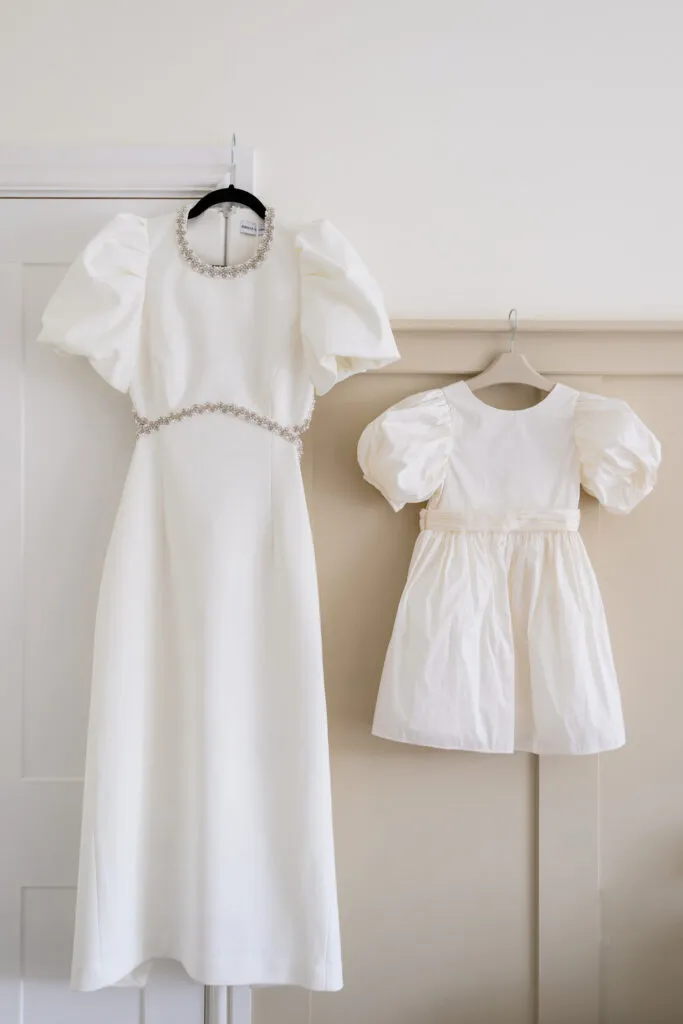 Bride’s wedding dress and flower girl dress hanging before the ceremony
