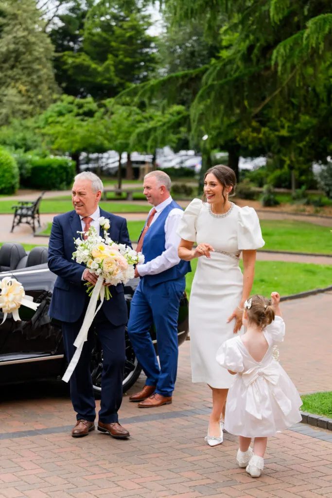 Bride walking into West Bridgford Park with family and flower girl after the ceremony