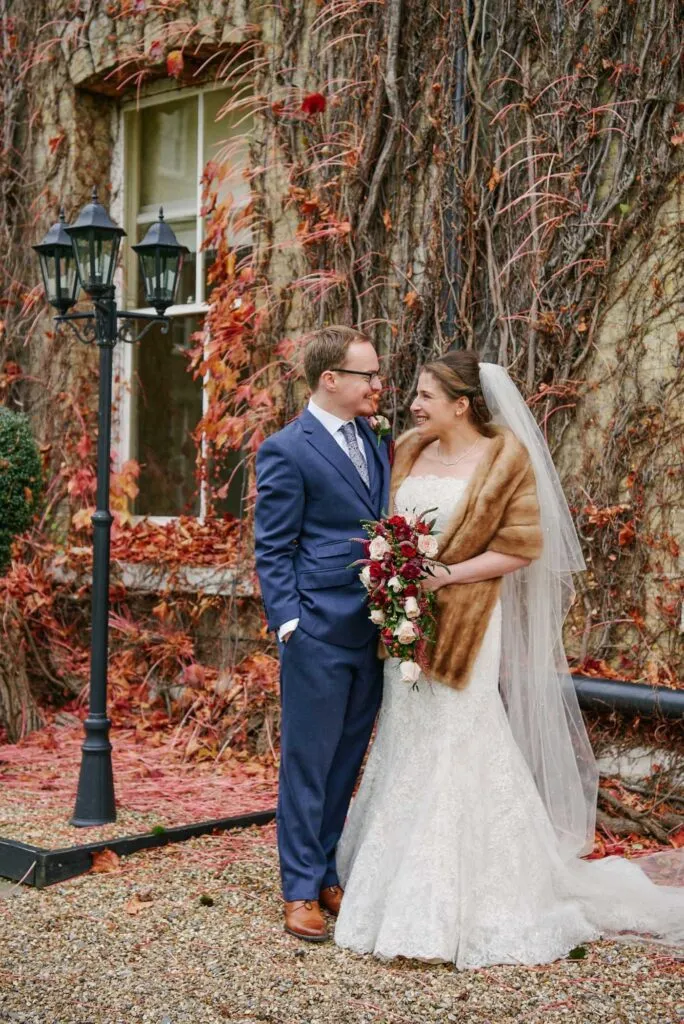 bride and groom smiling in front of red autumn leaves at fun winter wedding