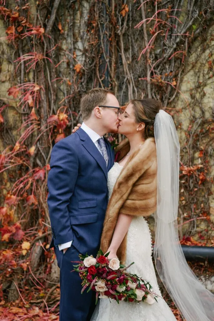 bride and groom kissing in front of red autumn leaves at Beaumont Estate