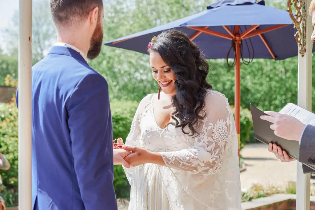 bride putting ring on groom's finger during an outdoor Pippley Walled Garden wedding.